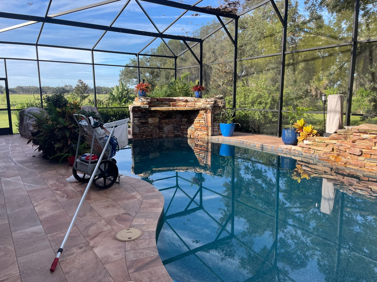 Amanzi Pool Service cleaning equipment beside a sparkling screened-in backyard pool