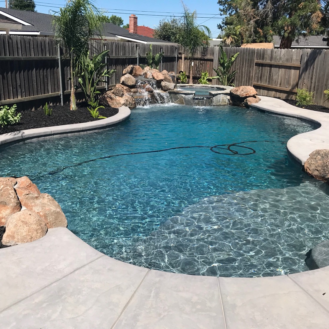 Sparkling clean backyard pool with waterfall feature maintained by Amanzi Pool Service